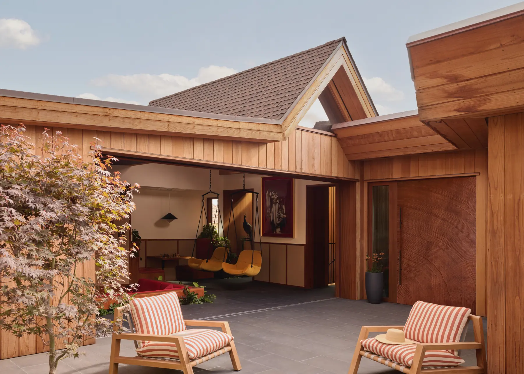 Timber-clad courtyard of a contemporary residence; open living area with hanging chairs, striped cushions, and potted plant.