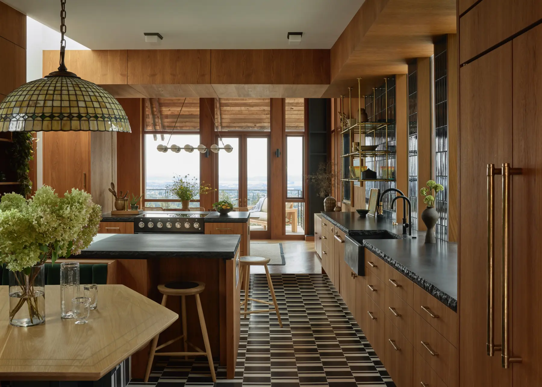 Interior kitchen with wood paneling and cabinetry, black granite counters, checkerboard floor, brass hardware, and city view through glass doors.