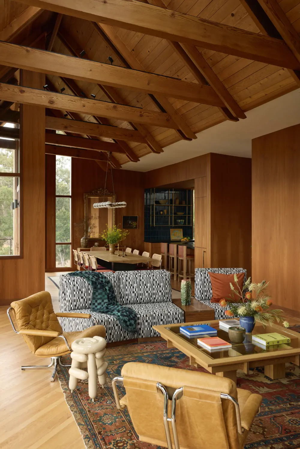 Interior living room with exposed timber roof trusses, walnut paneling, and a dining area with dark-blue tiled built-in cabinet backdrop.